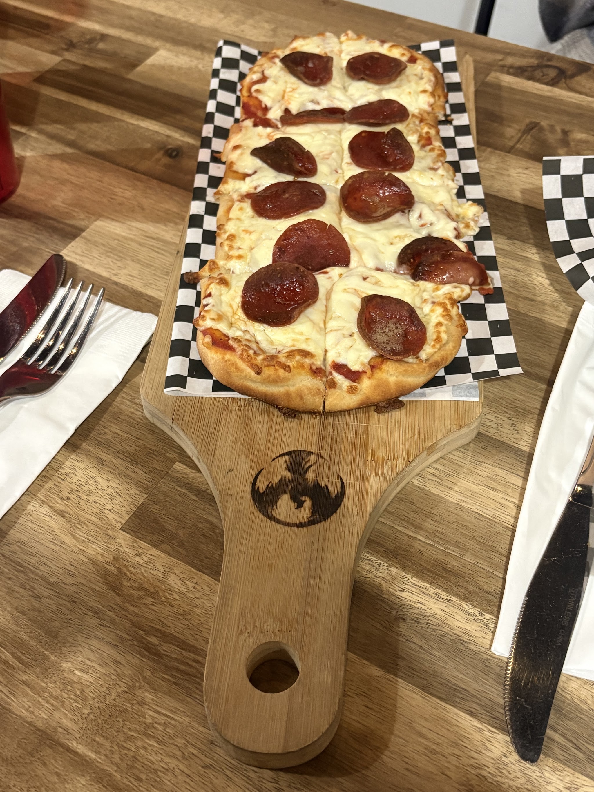 Pepperoni flatbread on branded dragon paddle board with checkered deli paper
