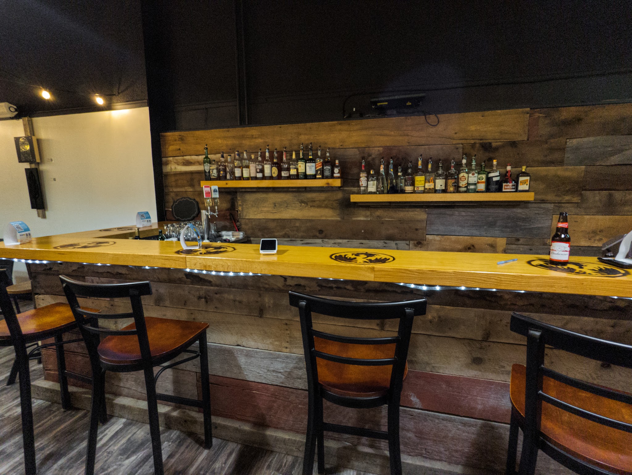 Ignition Eatery bar area with reclaimed wood wall, bottles, and bar stools